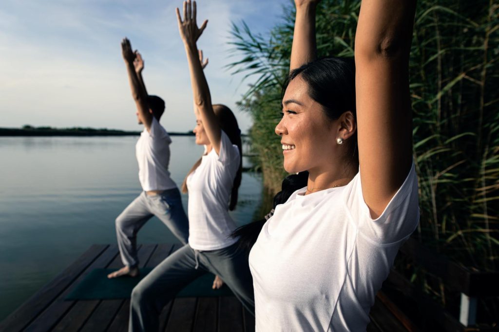 Group of people doing yoga exercises by the lake at sunset.